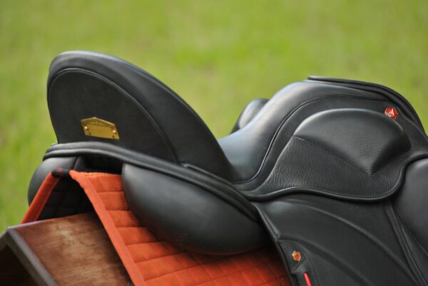 A close up of an Albion Revelation Red Label Dressage saddle on a grassy field.