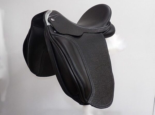 A black Ryder Baroque Dressage saddle hanging on a wall.