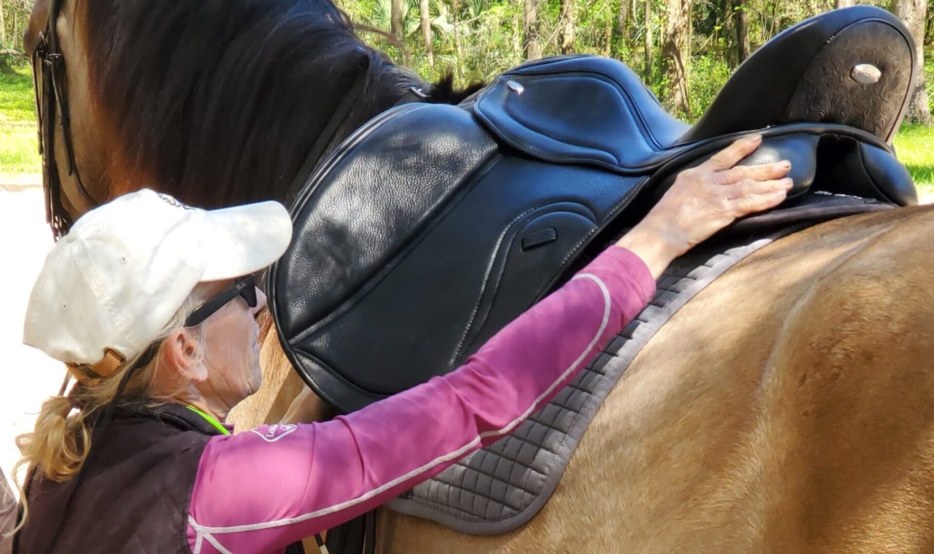 A woman wearing a hat and pink jacket expertly holding a saddle on a horse, showcasing her exceptional skill in custom saddle sales and services.