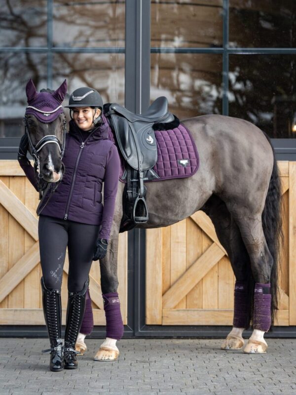 A woman is standing next to her horse in a pair of Lemieux Freya Breeches.