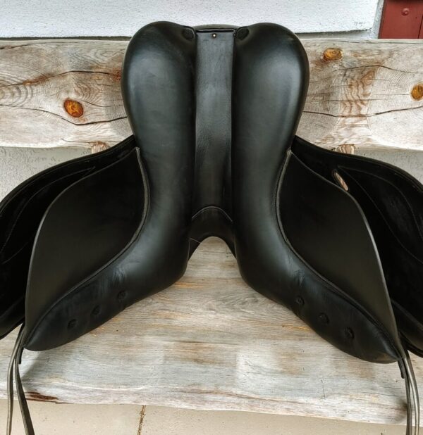 A pair of IKONIC ‘PRO’ Evolution Dressage UC245 saddles on a wooden bench.