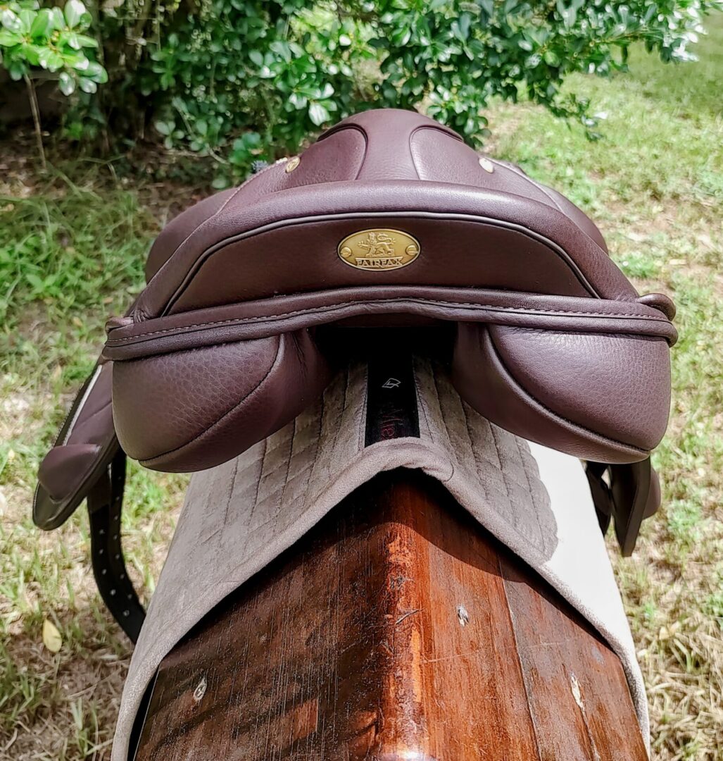 Brown saddle on a wooden bench outdoors.