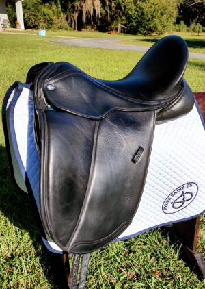 Black dressage saddle on white pad outdoors.