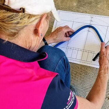 A woman providing saddle fit services, sitting on the ground and drawing on a piece of paper.